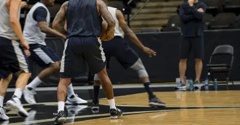 Anonymous veteran forward practices at centre as coach watches courtside.