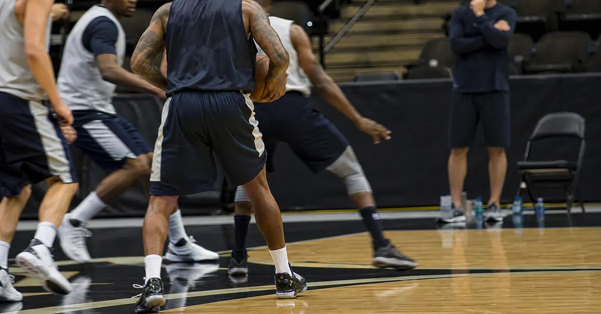 Anonymous veteran forward practices at centre as coach watches courtside.