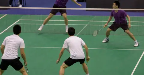 Anonymous badminton doubles athletes compete during an indoor tournament match.