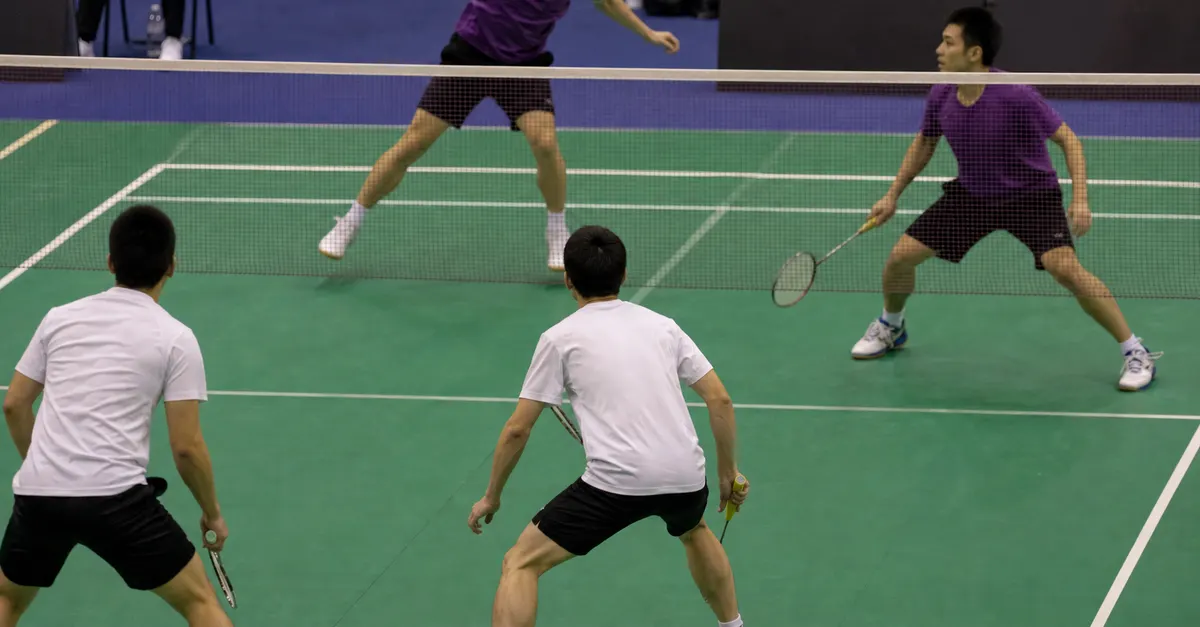 Anonymous badminton doubles athletes compete during an indoor tournament match.