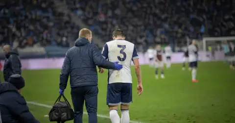 An anonymous footballer walks off the pitch with a trainer after injury.
