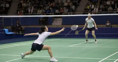 Two anonymous badminton players contest a point during an indoor final.