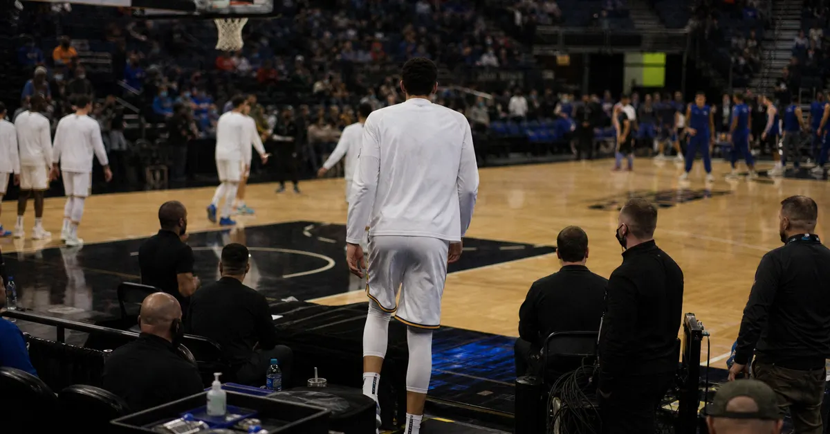 Anonymous basketball forward steps onto court as players warm up nearby