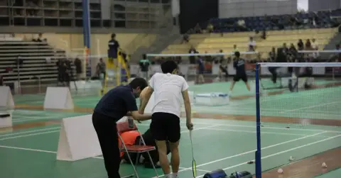 An injured badminton player pauses beside the court during a match.