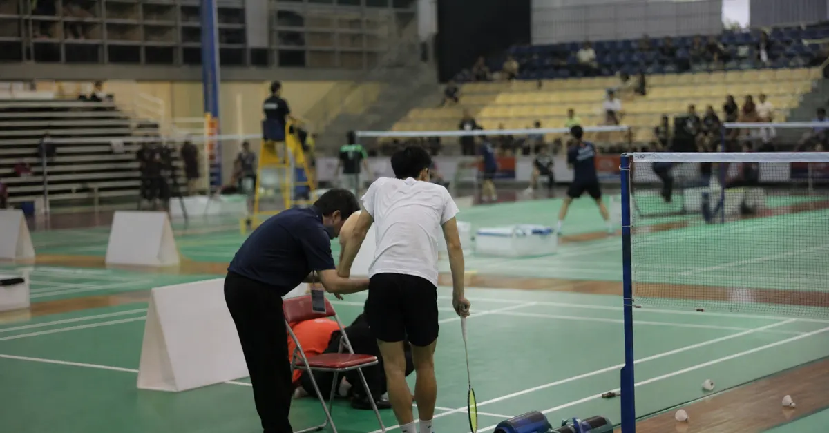 An injured badminton player pauses beside the court during a match.