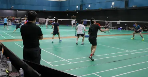 Anonymous badminton players train on adjacent courts as a coach watches.