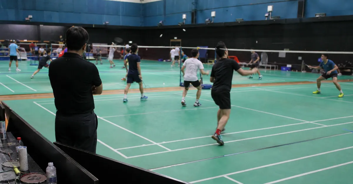 Anonymous badminton players train on adjacent courts as a coach watches.