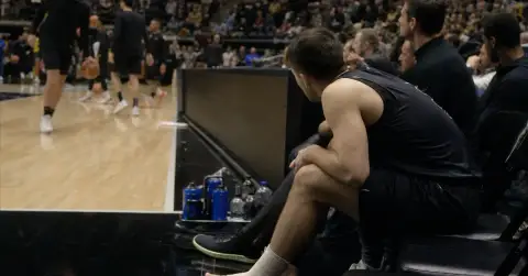 Anonymous basketball player with wrapped ankle watches teammates warm up.