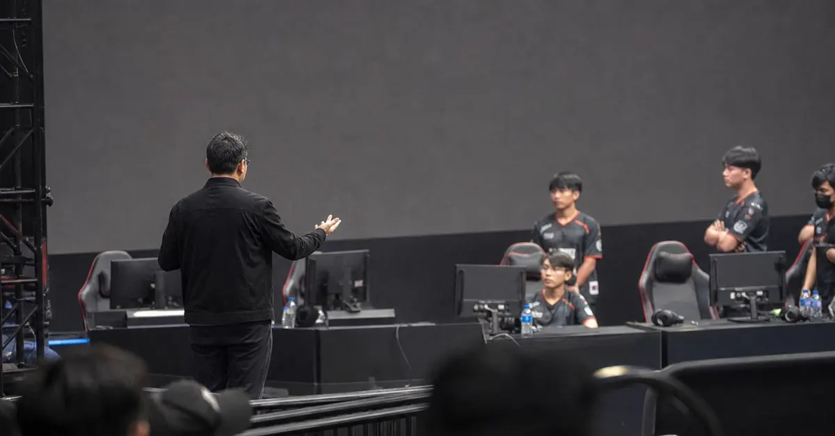 An esports official addresses staff beside gaming PCs and headsets