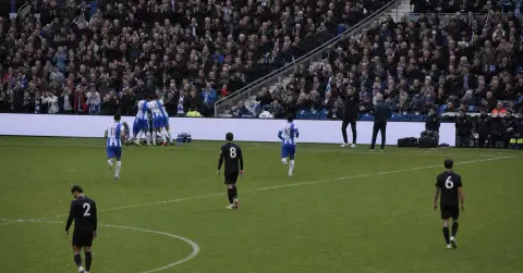 Anonymous footballers celebrate a goal as opponents return toward midfield.