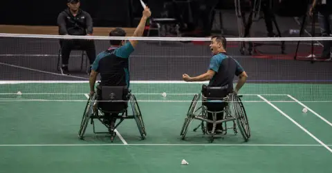 Two para-badminton partners celebrate a doubles victory beside the court.
