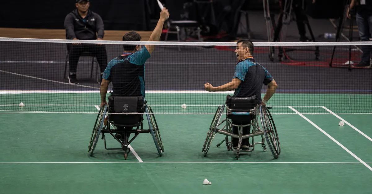 Two para-badminton partners celebrate a doubles victory beside the court.