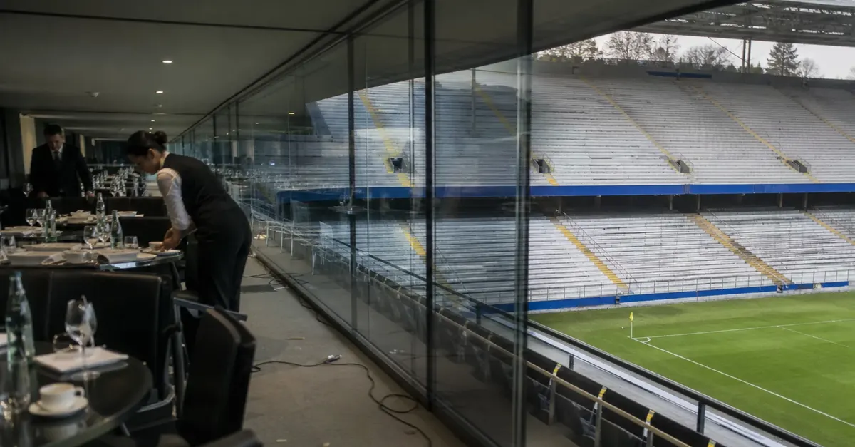 Empty football stadium showing a polished hospitality suite above ordinary stands.