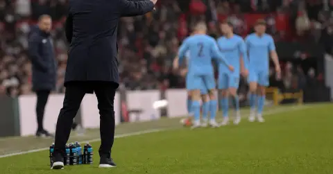 A coach urges anonymous players during a tense away football match.