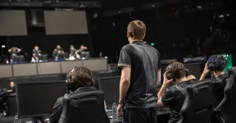 Anonymous esports players finish a match at PCs under arena lights.