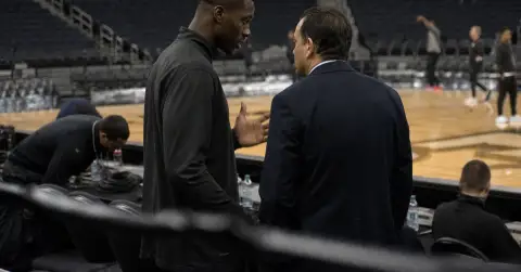 Anonymous basketball player and executive talk courtside in a quiet arena.