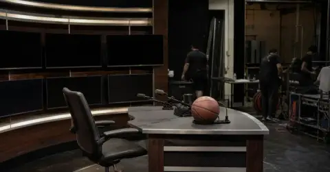 Empty basketball broadcast desk after a taping, with crew packing equipment
