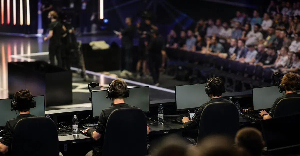 Anonymous esports players compete at computers in a crowded tournament arena.
