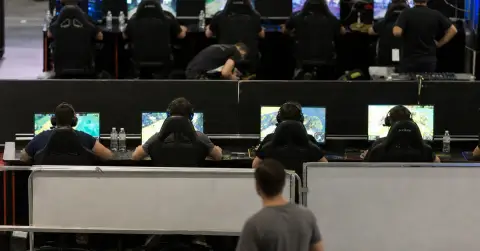 Two esports competitors play at separate partner qualification stations in an arena.