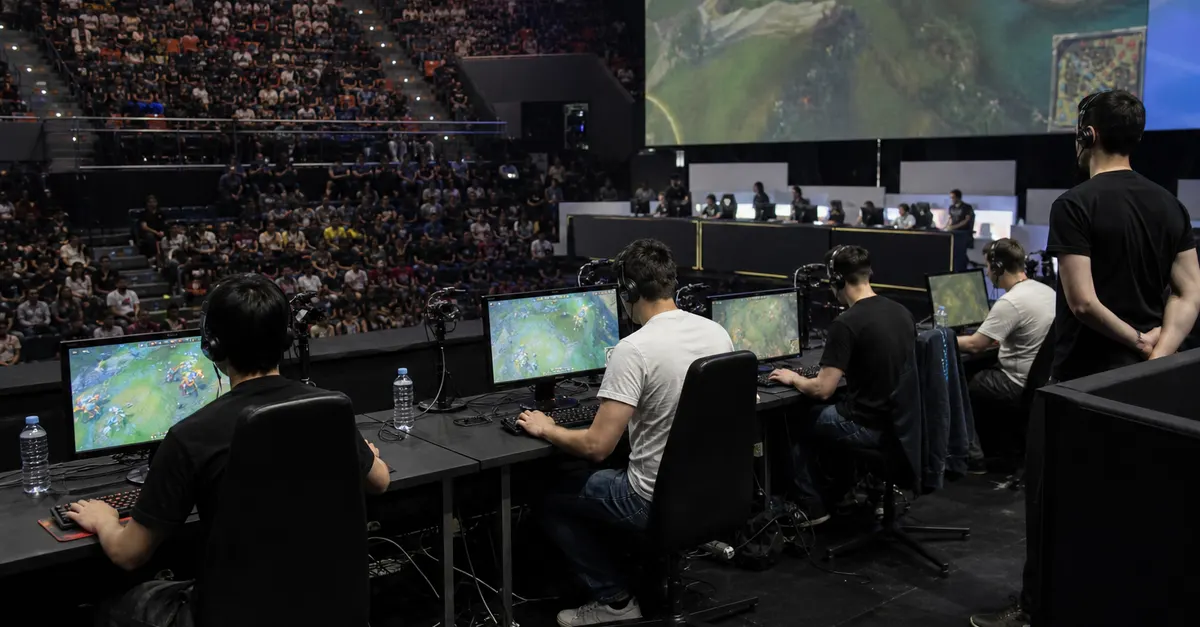 Anonymous esports finalists compete at gaming stations beneath arena screens.