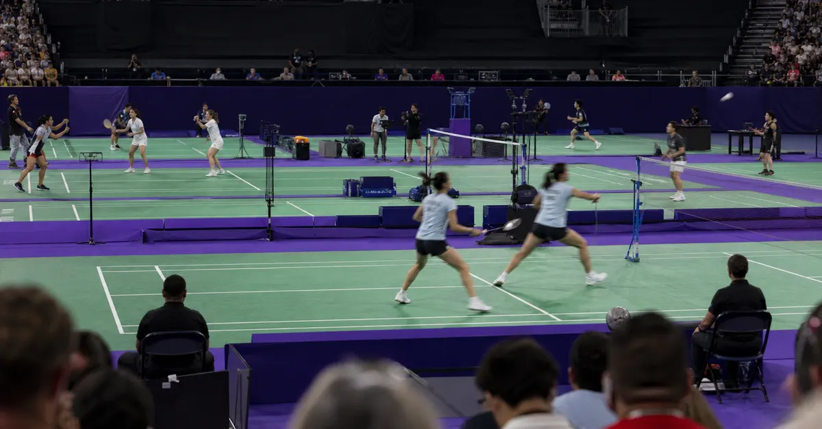 Malaysian badminton doubles players compete beneath arena lights during a major tournament.