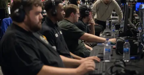 Adult players prepare at a modest esports tournament beside gaming PCs.