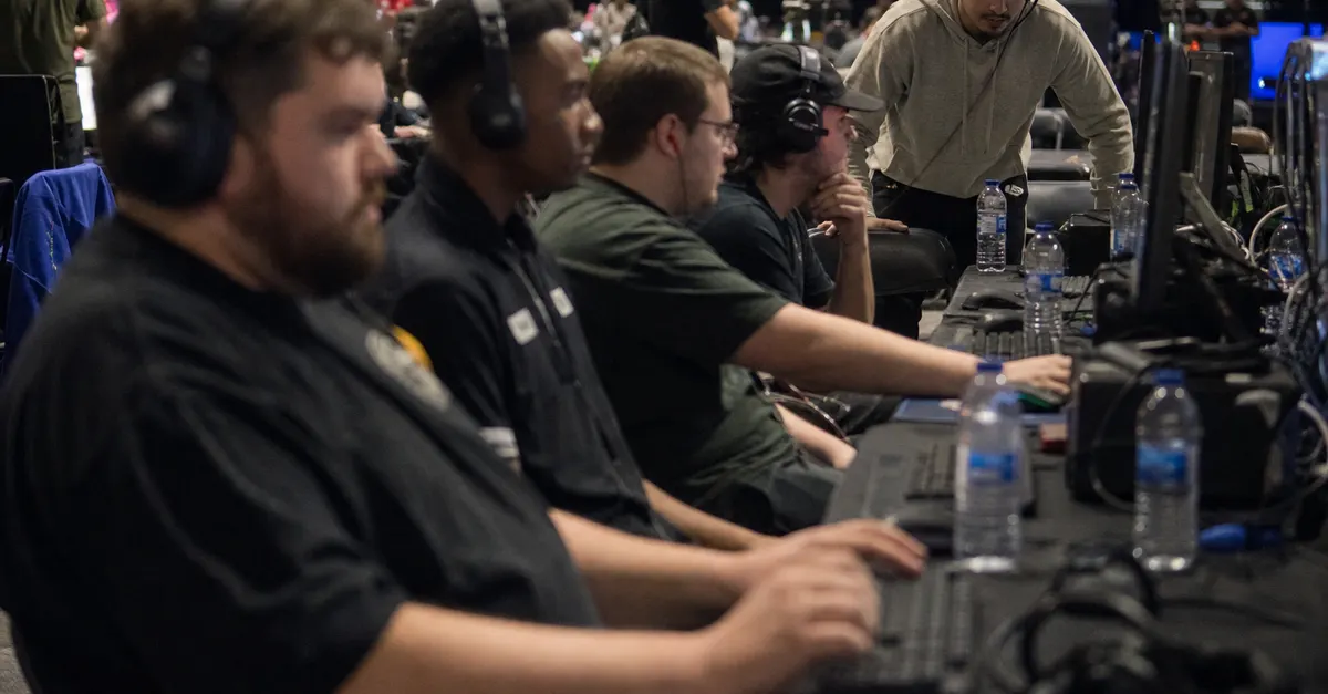 Adult players prepare at a modest esports tournament beside gaming PCs.