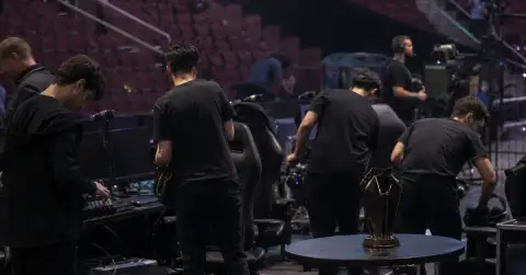 Anonymous esports players pack equipment beside empty gaming chairs after a tournament
