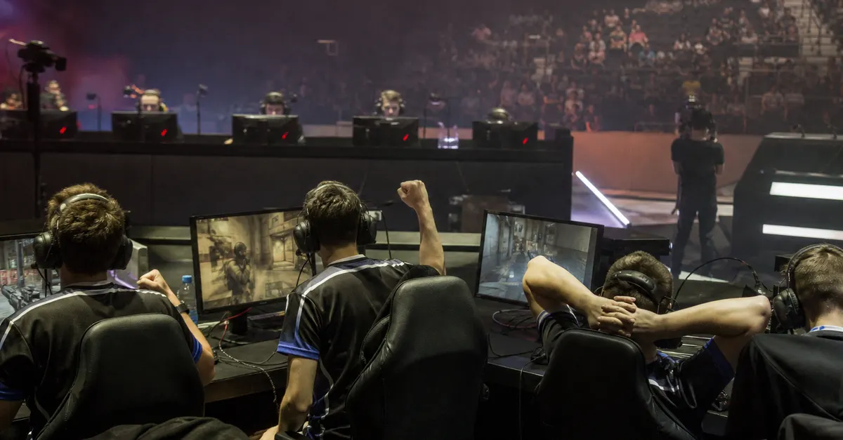 Anonymous esports players compete at gaming PCs in a crowded arena.