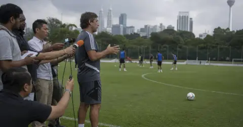 Anonymous football analyst discusses long shots beside a Kuala Lumpur training pitch.