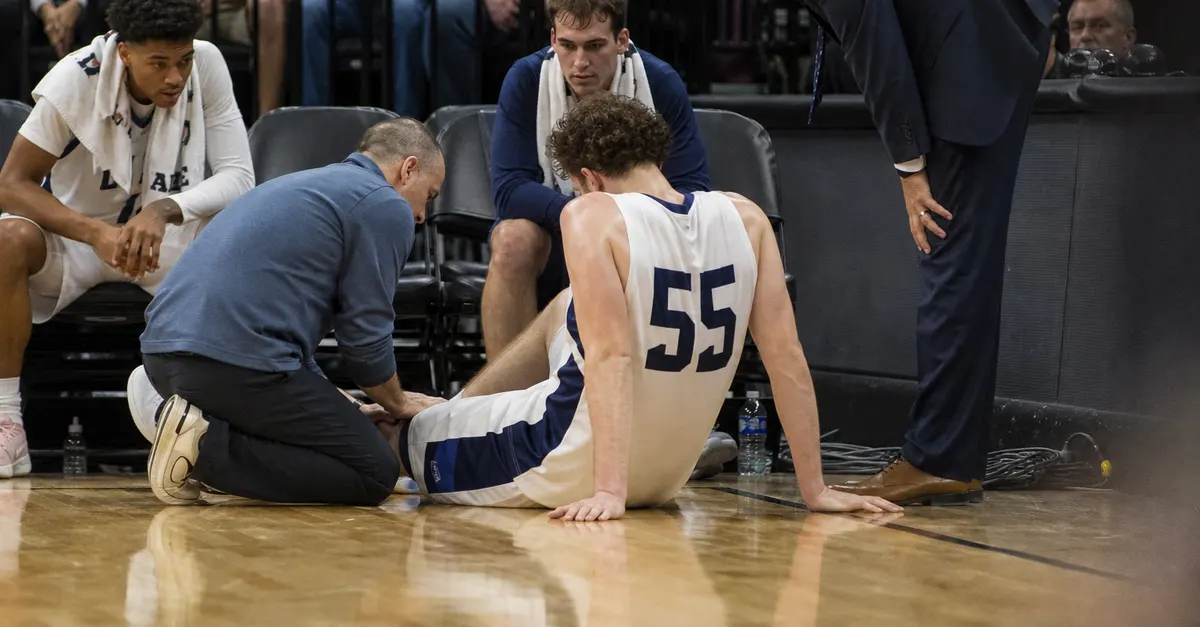 Injured basketball player sits courtside as staff check his lower leg