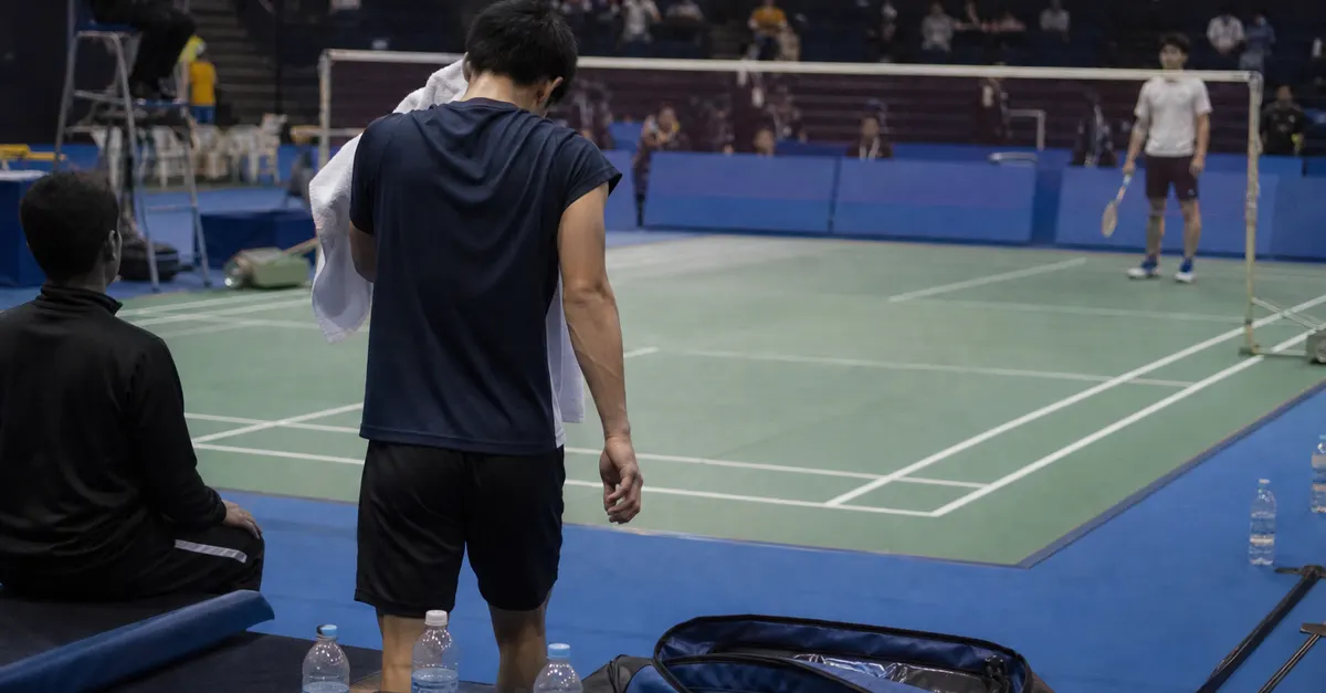 Exhausted badminton player pauses between points during an indoor match.