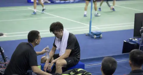 Exhausted badminton player sits courtside after a tournament match