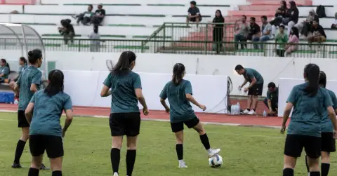 Women footballers warm up on a modest stadium pitch before a match.