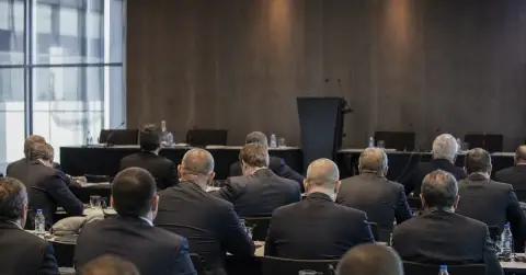 Anonymous football officials gather in a plain conference room during governance uncertainty.