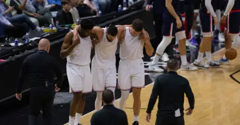 An injured basketball player is helped off court by teammates.