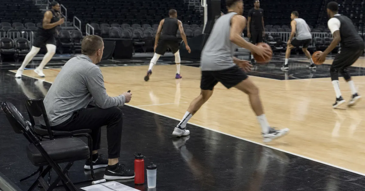 Anonymous basketball players practice on a court beside waiting staff.