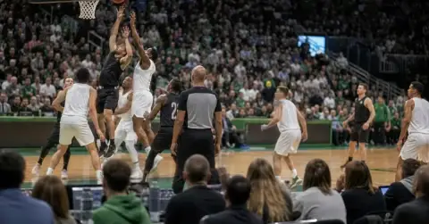 Anonymous basketball players contest a rebound in a crowded arena.