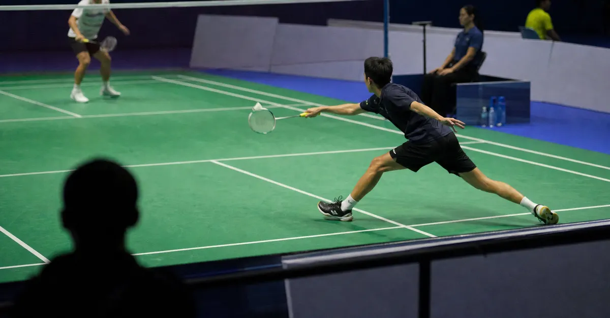 A badminton player lunges forward during a tense indoor singles rally.