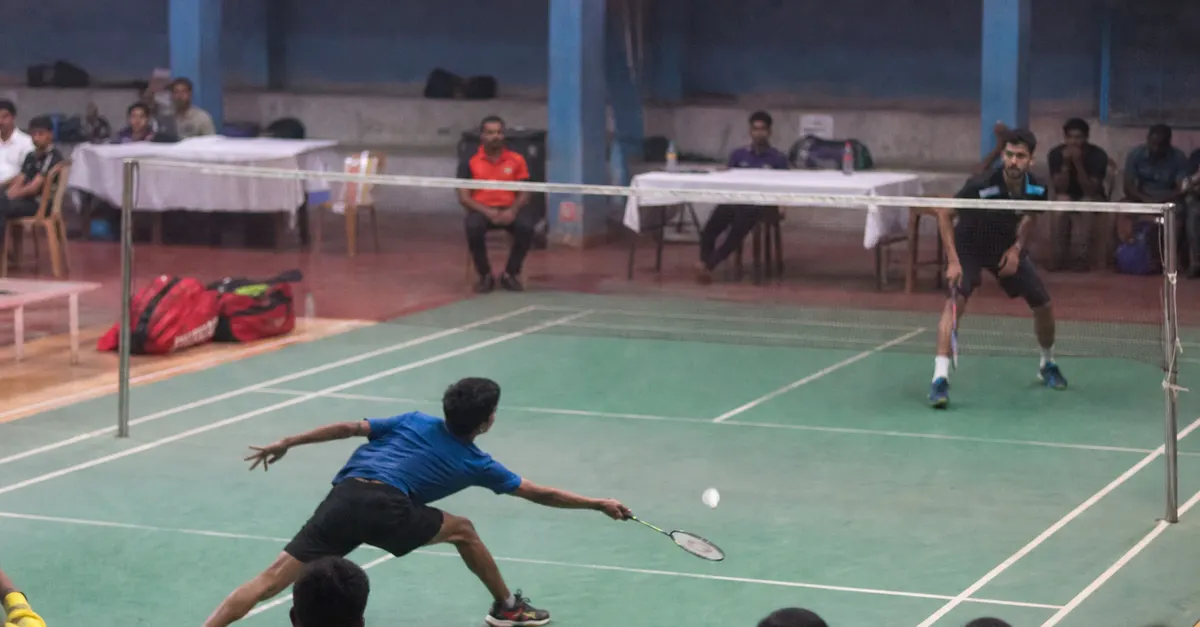 Two badminton players contest a rally inside an indoor arena.