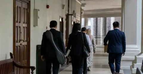Anonymous adults leave a courthouse corridor, one carrying a badminton racket bag.