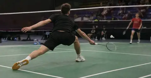 Anonymous badminton player reaches for shuttle during indoor tournament match.