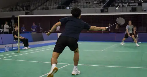 Anonymous badminton player reaches for a shuttle during an indoor match