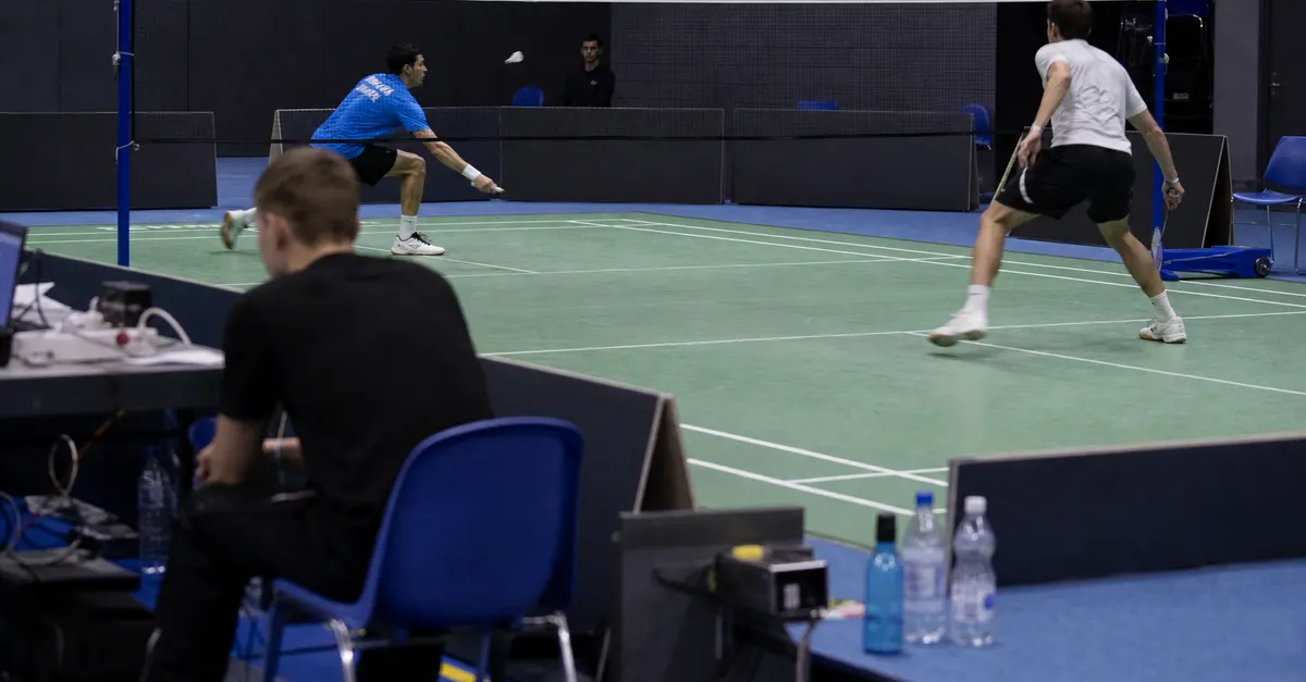 Anonymous badminton players rally during an indoor tournament match in Germany.