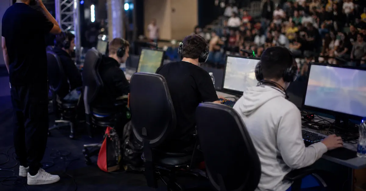 Anonymous esports players compete onstage beneath arena lights, with equipment and spectators.