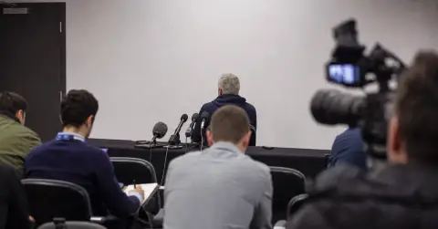 Anonymous football coach speaks at a press conference amid cameras.