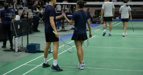 Anonymous badminton athletes celebrate a mixed-team victory beside the net