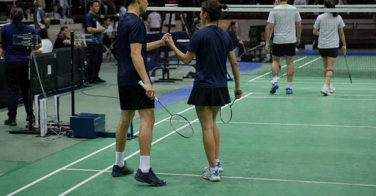 Anonymous badminton athletes celebrate a mixed-team victory beside the net
