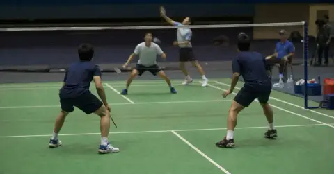 Four badminton players prepare for a doubles rally in an indoor arena