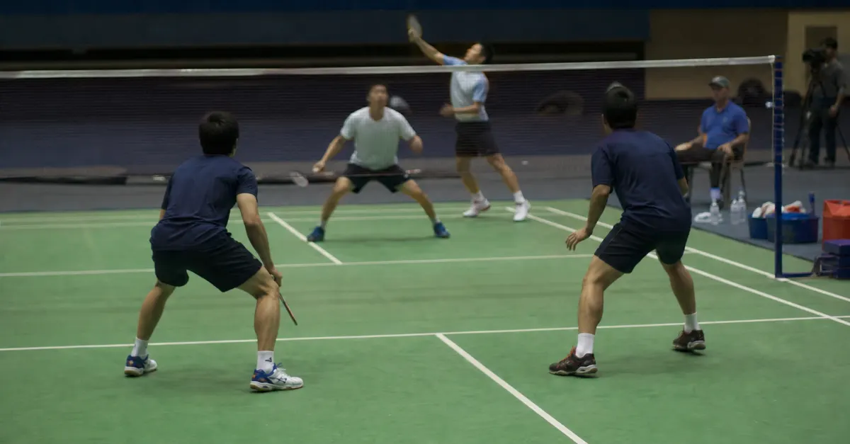 Four badminton players prepare for a doubles rally in an indoor arena